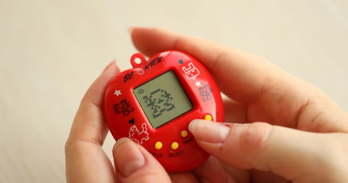 Joc retro Tamagotchi cu breloc pentru animale de companie, într-o cutie din plastic roșu, în mâinile unei femei, prim-plan