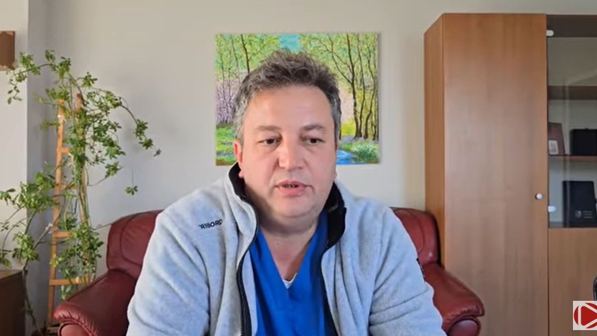 Managerul Spitalul Județean de Urgență din Ploiești, dr. Sebastian Toma, îmbrăcat un cu halat albastru și hanorac gri, vorbește despre situația dificilă din spital, în spatele lui se vede un tablou, în stânga o floare, iar în dreapta este o bibliotecă