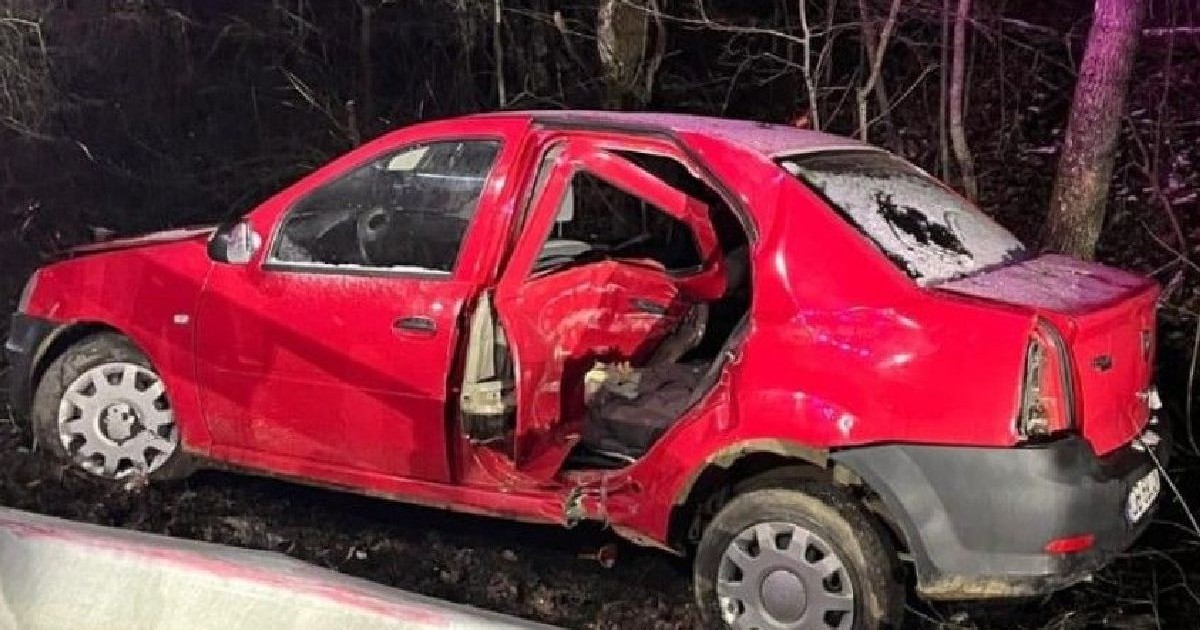 O berlină roșie, grav avariată, cu luneta spartă și oglinda laterală lipsă, după un accident.