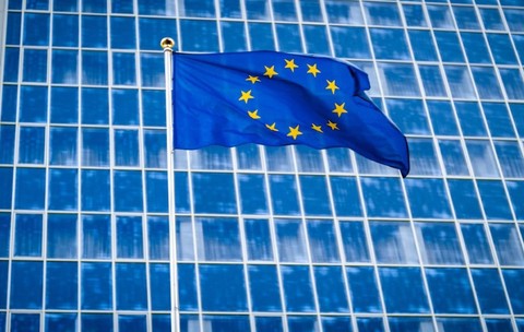 Imagine creativă cu steagul Uniunii Europene arborat în fața unei clădiri administrative din Bruxelles cu geamuri de culoare albastră