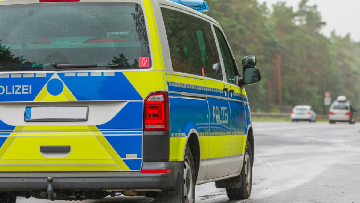 Vedere laterală a mașinii de poliție germane. Partea pasagerului a vehiculului pe autostradă, pe vreme ploioasă, cu inscripția „Police” pe caroserie, vopsită în albastru și galben.