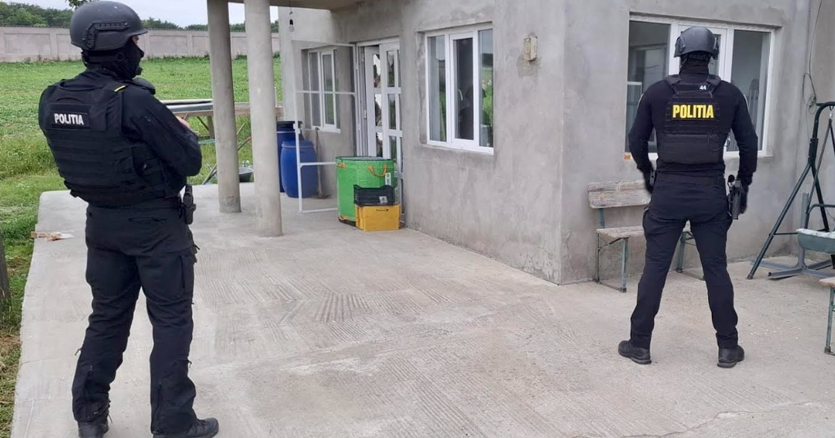 Doi polițiști stau în fața unei case din Corbasca, județul Bacău, care urmează să fie percheziționată