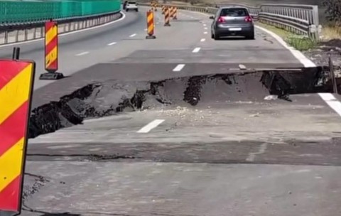 O porțiune de asfalt surpată pe o autostradă, unde zona afectată este semnalizată cu balize rutiere temporare de avertizare.