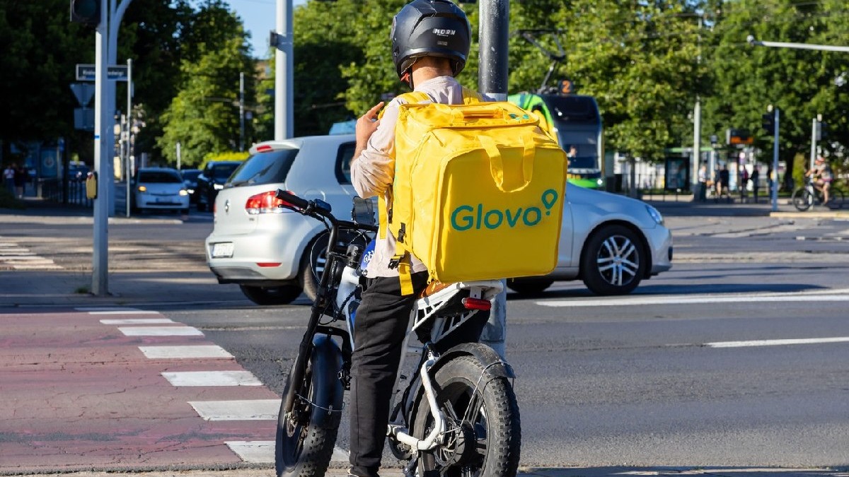 Poznan, Polonia - 30 iunie 2025: Curierul Glovo, cu rucsacul său galben distinctiv, așteaptă pe o bicicletă electrică la o intersecție aglomerată.
