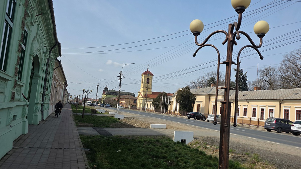 Imagine de ansamblu cu o stradă din localitatea Lovrin iar în lateral se vede biserica.