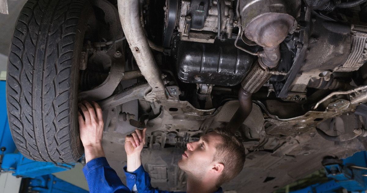 Un mecanic în salopetă albastră repară o mașină, stând sub ea