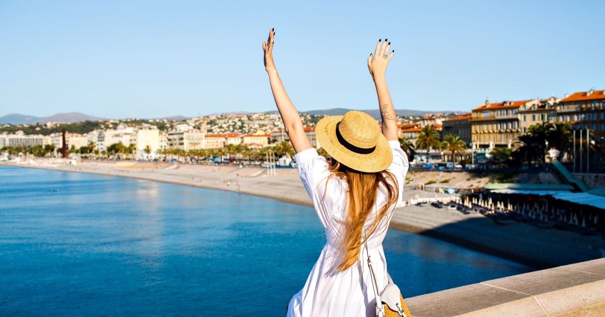Touristic picture of happy elegant woman posing back, put her hand in the air and enjoying amazing view in France Cannes beach, traveling goals, elegant glamour clothes, summertime.
