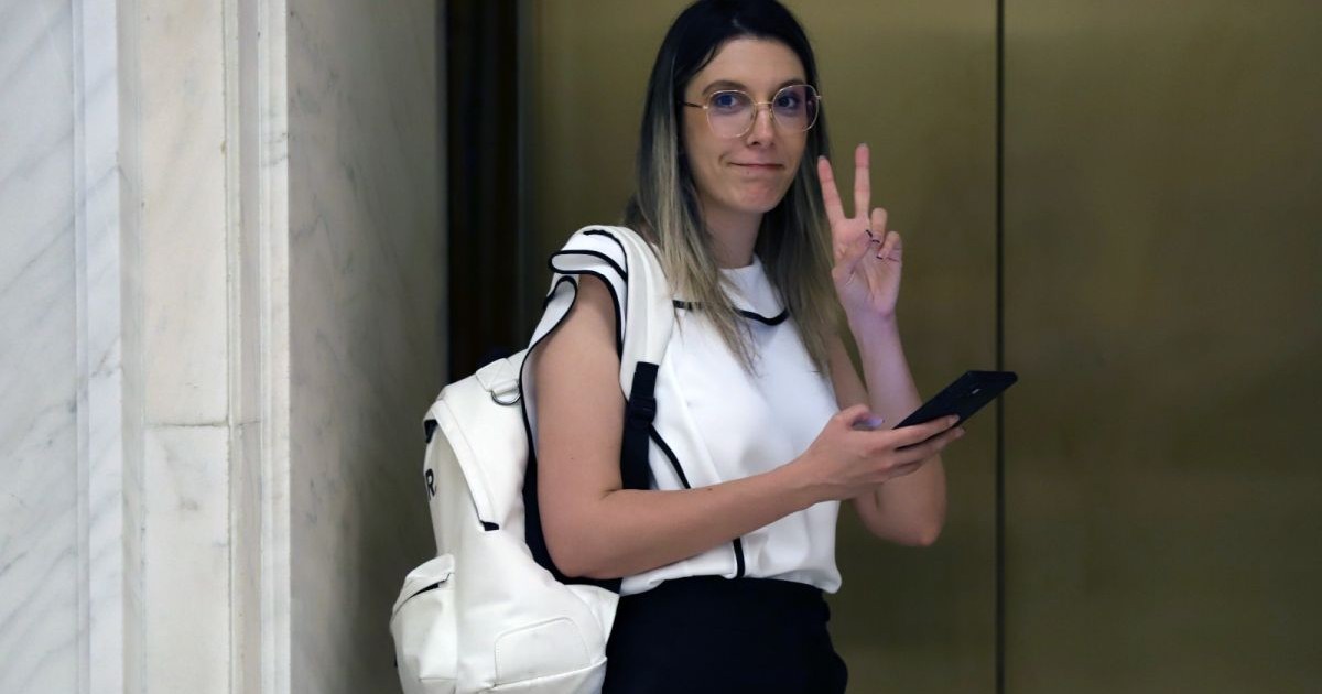 Ministrul Mediului, Diana Buzoianu, îmbrăcată cu o bluză albă și ghiozdan alb în spate, arată semnul victoriei cu mâna, în timp ce așteaptă liftul din Parlament și se uită spre fotograf, București, 5 ianuarie 2026