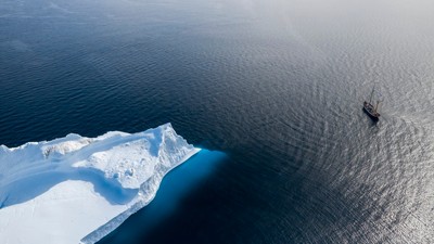 Ship sailing past arctic iceberg on sunny Atlantic Ocean Greenland