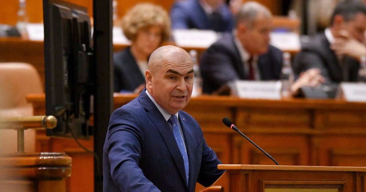 Premierul Ilie Bolojan le vorbește parlamentarilor de la pupitru, îmbrăcat într-un costum bleumarin