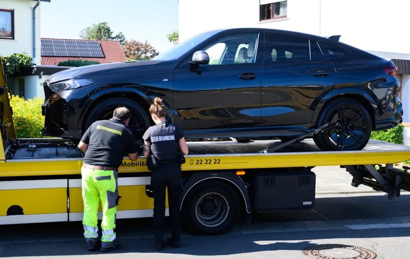 Un autoturism BMW negru încărcat pe platforma unei mașini de tractare, în timp ce un operator și o femeie agent fixează vehiculul.