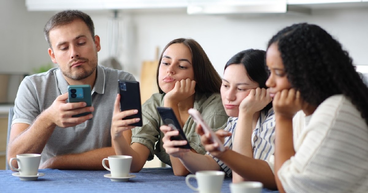 Prietenii plictisiți își folosesc telefoanele inteligente în bucătăria de acasă