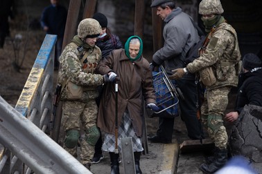 O vârstnică din Irpin, ajutată de soldați ucraineni să traverseze podul distrus pentru a ieși din oraș | Foto: Hepta