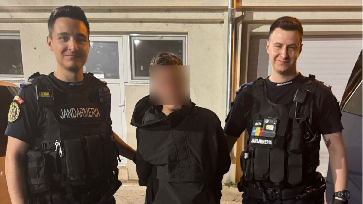 Doi jandarmi, îmbrăcați în uniforme, îl țin de mâini pe un suspect, îmbrăcat în negru și cu fața blurată