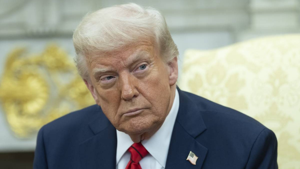 Donald Trump, în Biroul Oval, îmbrăcat într-un costum de culoare albastra cu o cravată roșie și insigna steagului american prinsă pe rever