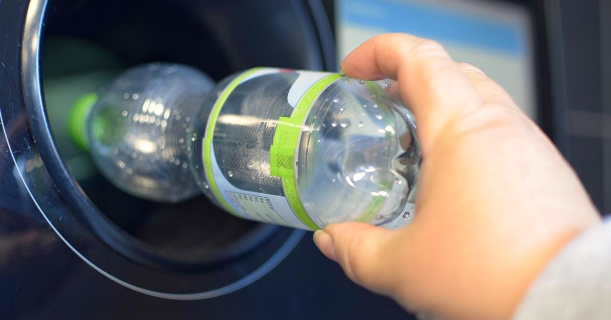 O femeie pune o sticlă de plastic într-un aparat de reciclat.