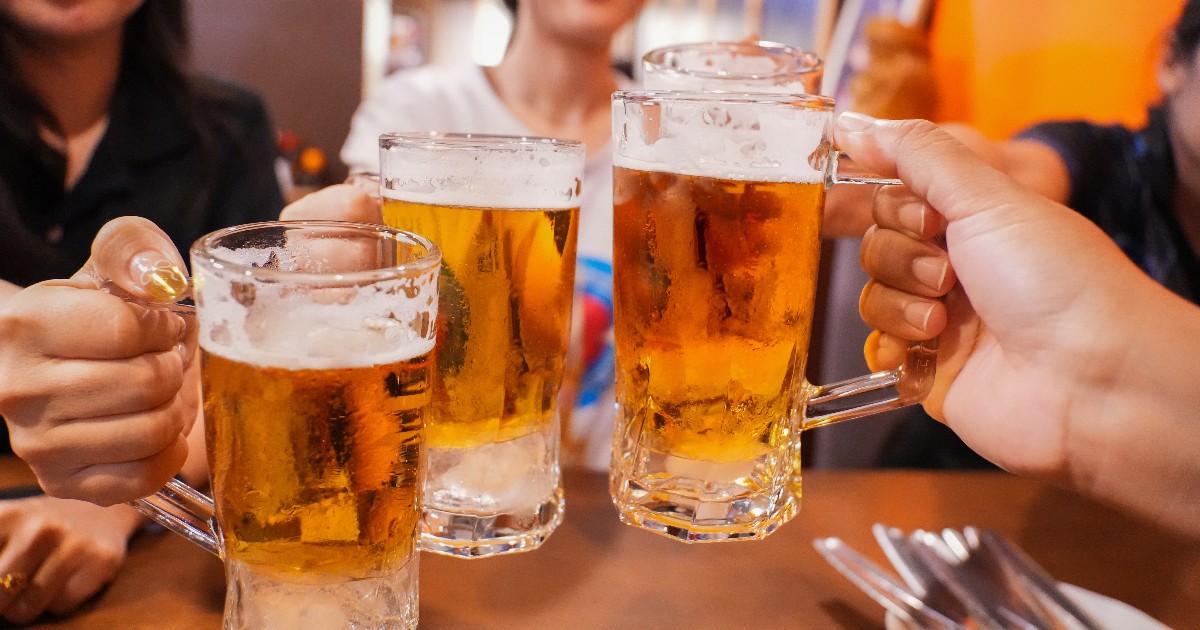 Imaginea surprinde mai multe persoane ciocnind halbe cu bere într-un local, într-o atmosferă relaxată și convivială. Paharele pline cu bere sunt ridicate pentru un toast, sugerând un moment de socializare între prieteni.