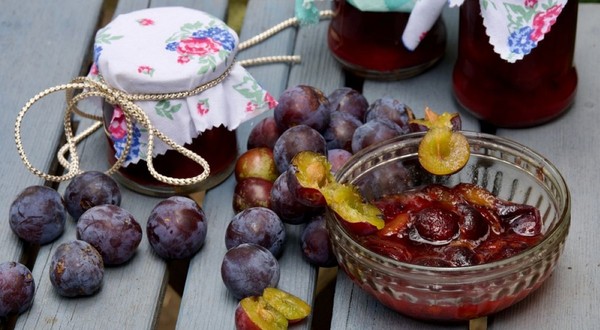 Un bol cu dulceață de prune, prune întregi și borcane de gem pe o masă de lemn