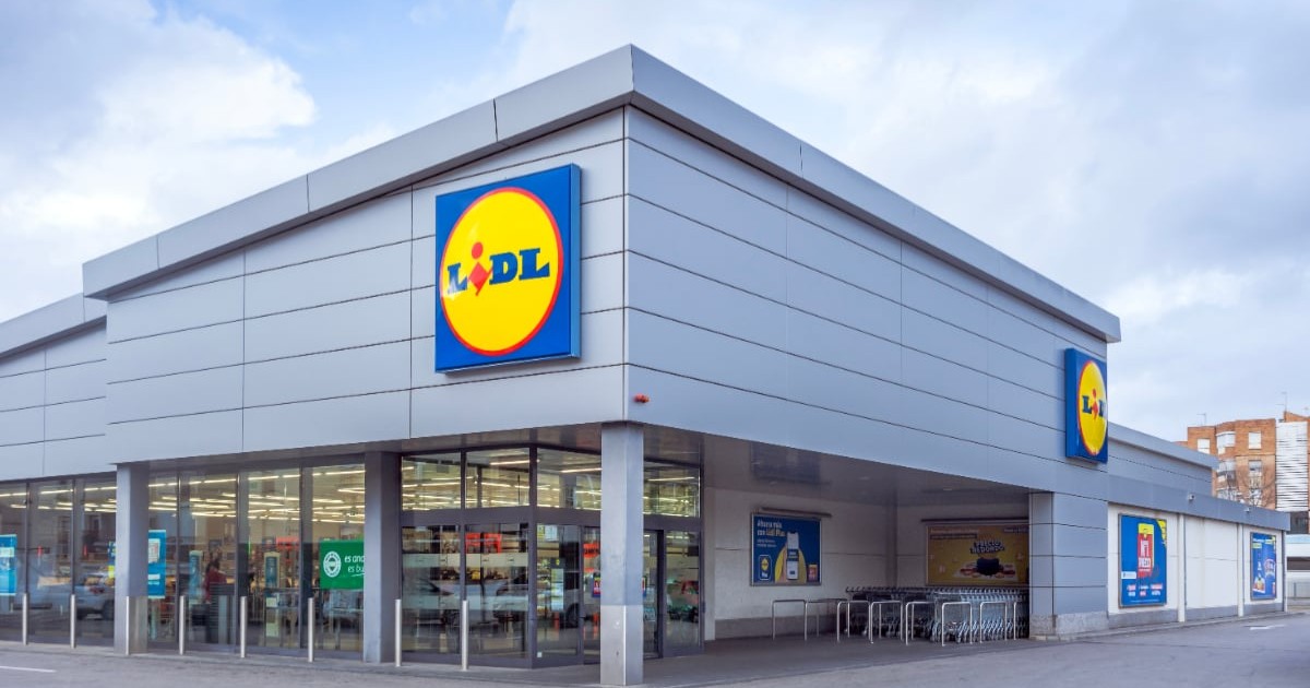 Intrarea într-un magazin Lidl, parcarea este goală și în interiorul supermarketului lumina este aprinsă