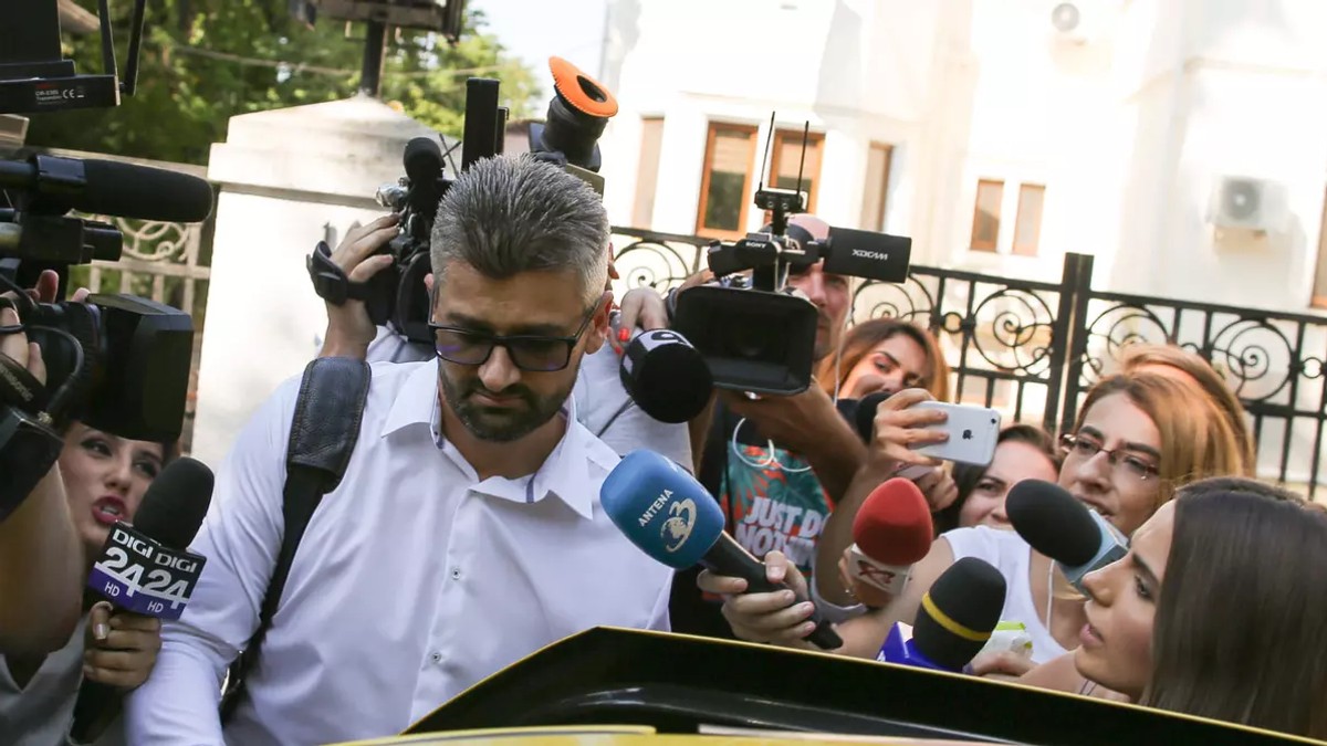 Un barbat imbracat in camasa alba este inconjurat de reporteri