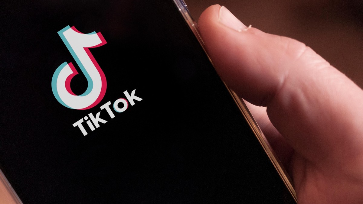 Imagine cu mâna unui bărbat în care se află un telefon. Pe ecran este afișat logo-ul TikTok