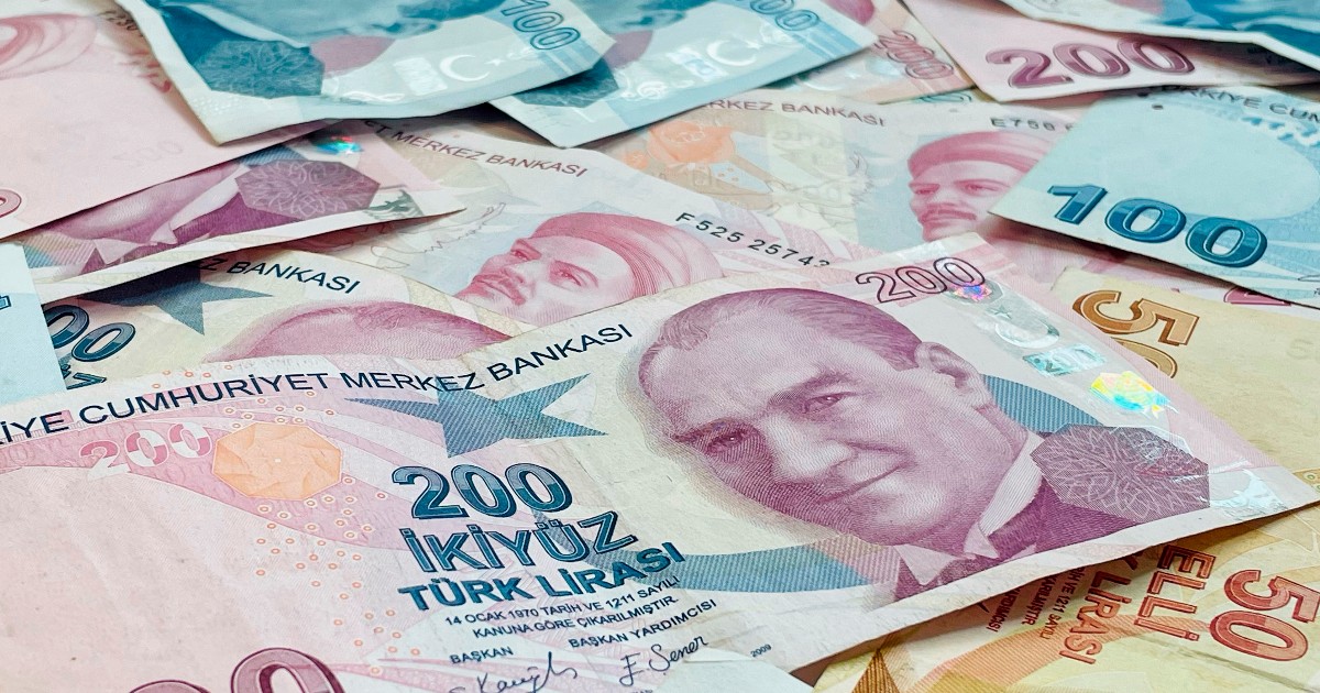 Bancnote lira turceasca de diferite valori așezate pe o suprafață. Culorile predominante sunt nuanțe de roz, albastru și bej