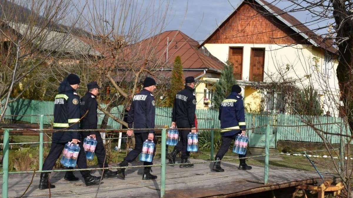 Mai mulți pompieri au sticle de apă cu etichete roză în mână, merg pe o alee, printre case, în Prahova şi Dâmboviţa, 2 decembrie 2025