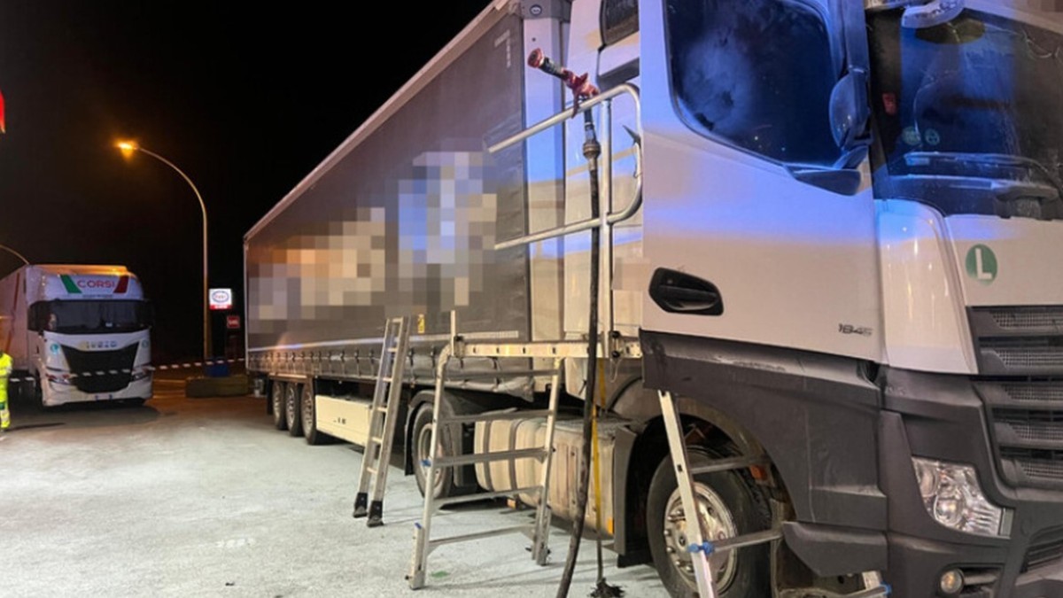 Un autotren alb oprit pe timp de noapte într-o parcare sau stație de serviciu, având o platformă metalică și o scară instalate lângă cabină pentru acces la înălțime.