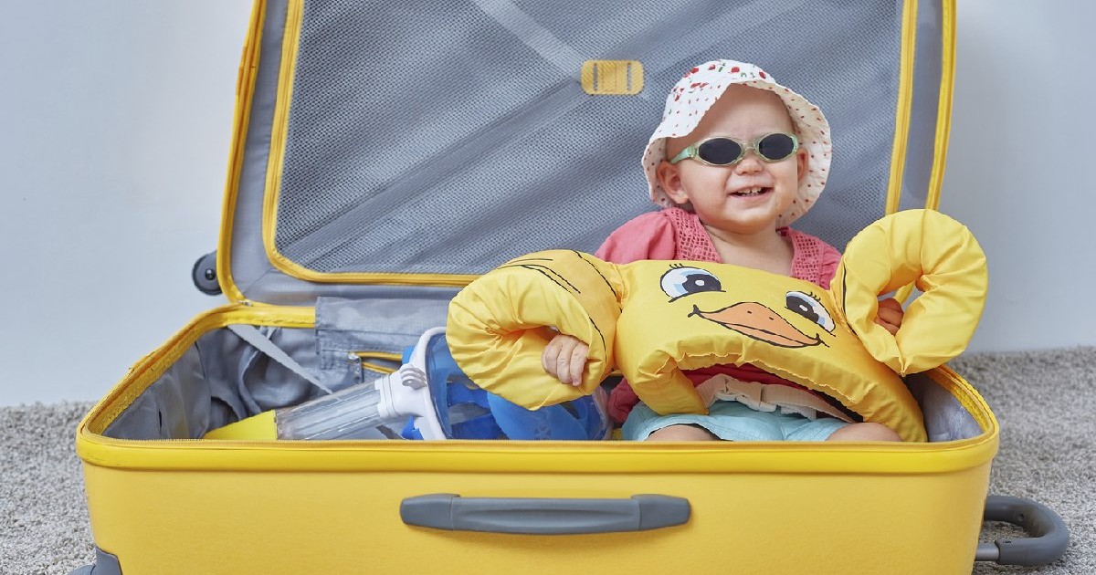 Bebșus cu palarie si ochelari la ochi, într-o valiză galbenă cu lucruri pentru o vacanță la mare
