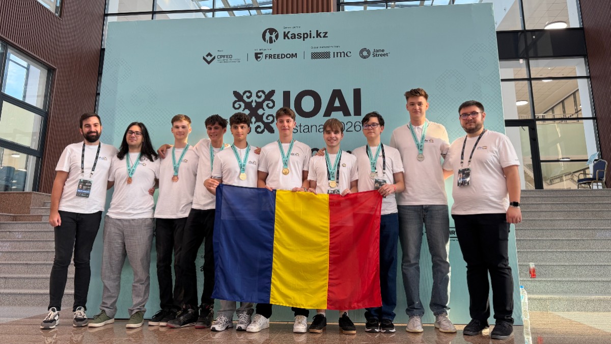 În imagine este surprins lotul României la Olimpiada Internațională de Inteligență Artificială (IOAI), alături de coordonatori, după obținerea medaliilor, având în față drapelul României. Fotografia ilustrează performanța elevilor români în competiția internațională și succesul echipei la ediția din 2026.