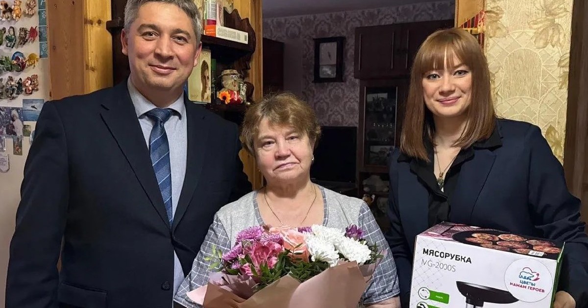 Un bărbat și două femei. O femeie ține în mână un buchet de flori, iar cealaltă o mașină de tocat.