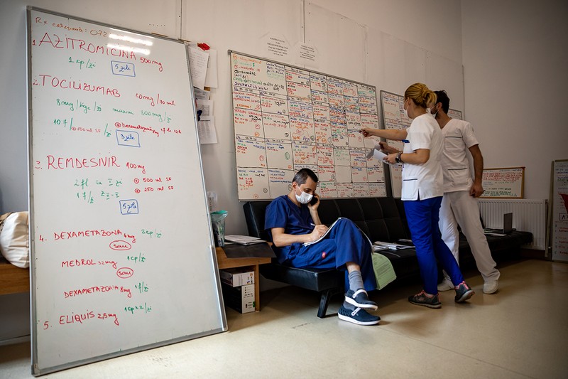 Doi medici consultă lista pacienților internați. Pe panoul din stânga sunt scrise medicamentele folosite în tratarea bolii.