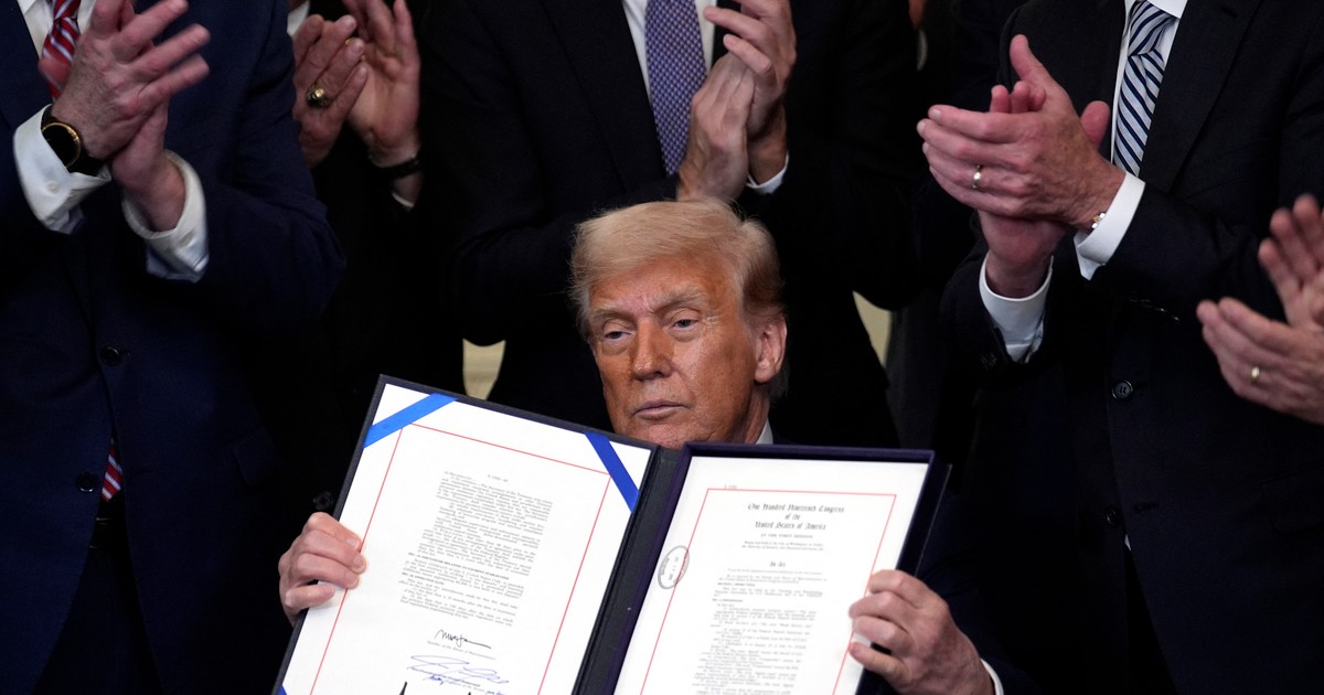 Donald Trump (în mijloc) surprins după semnarea legii GENIUS. Pe fundal se văd mai multe mâini care aplaudă