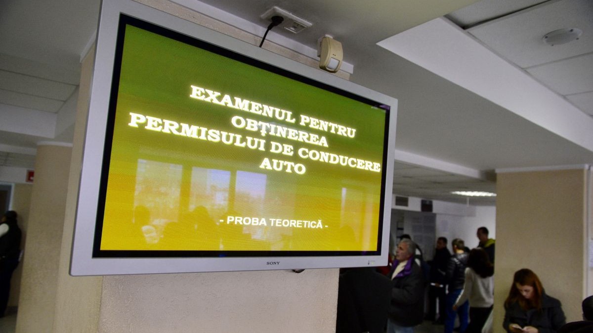 Mai mulți oameni stau la coadă, în sediul Direcției Regim Permise de Conducere și Înmatriculare a Vehiculelor (DRCPIV), pentru a susține proba teoretică la examenul auto