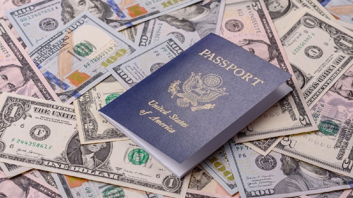 Un pașaport american cu coperți bleumarin, asezat pe diverse bancnote dolar american