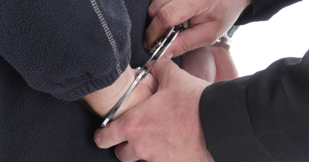 Prim-plan cu mâinile polițistului care încătușează un bărbat