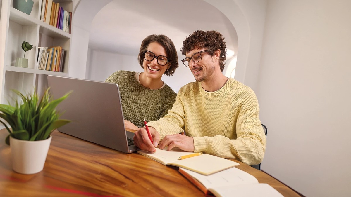 Femeie și bărbat purtând ochelari de vedere, lucrând împreună la laptop