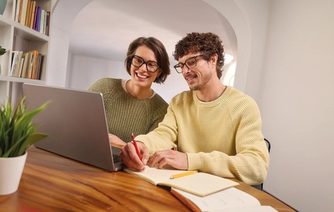 Femeie și bărbat purtând ochelari de vedere, lucrând împreună la laptop