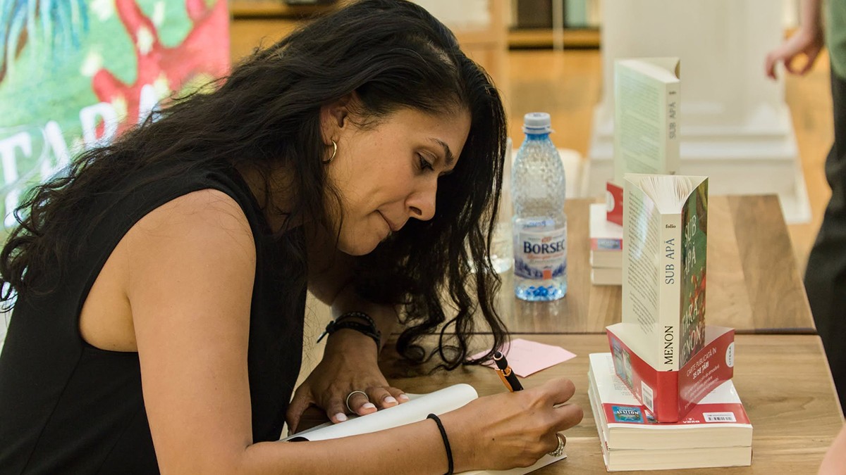 O tanara bruneta imbracata intr-o rochie neagra scrie un autograf pe o carte