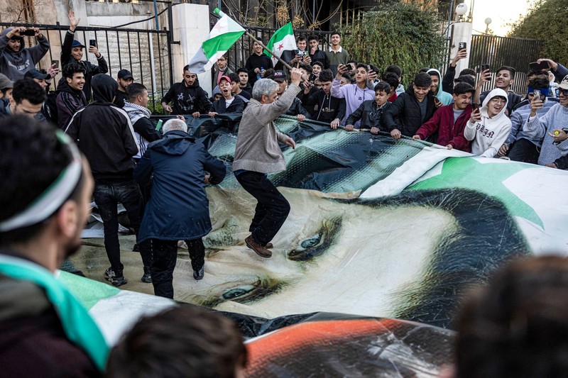 People stomp and tear apart a giant banner depicting the face of Syria's ouster president Bashar al-Assad during a rally near the Umayyad Square in central Damascus on December 13, 2024. Thousands rallied in central Damascus and in cities across Syria on December 13 to celebrate during the first Friday prayers since Assad's ouster. More than half a century of brutal rule by the Assad clan came to a sudden end on December 8, after a lightning rebel offensive swept across the country and took the capital.,Image: 946326063, License: Rights-managed, Restrictions: , Model Release: no