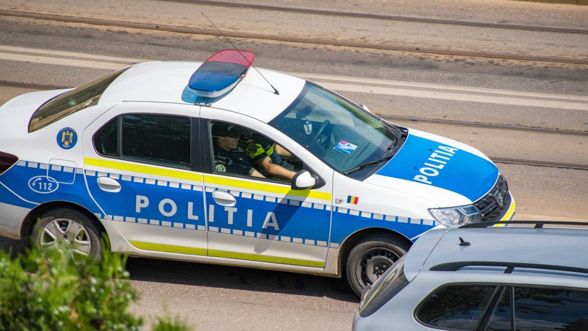 O mașină de Poliție în care stau doi polițiști în uniformă este parcată pe marginea drumului.