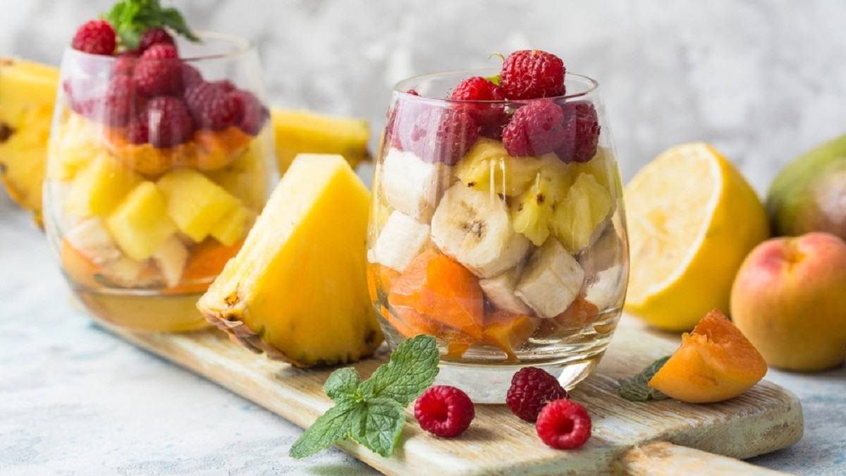 Fructe exotice și tropicale care îți dau energie: beneficii pentru sănătate și rețete - Salată de fructe cu banane, ananas și zmeură în pahare de sticlă pe un tocător de lemn