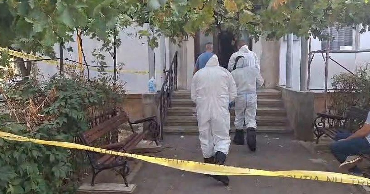 Anchetatori in costume albe intră intr-o scară de bloc din Drobeta Turnu Severin. In fundal se vede o banda galbena pusă de poliție la locul crimei
