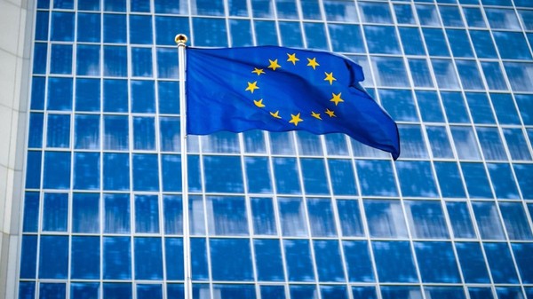 Imagine creativă cu steagul Uniunii Europene arborat în fața unei clădiri administrative din Bruxelles cu geamuri de culoare albastră