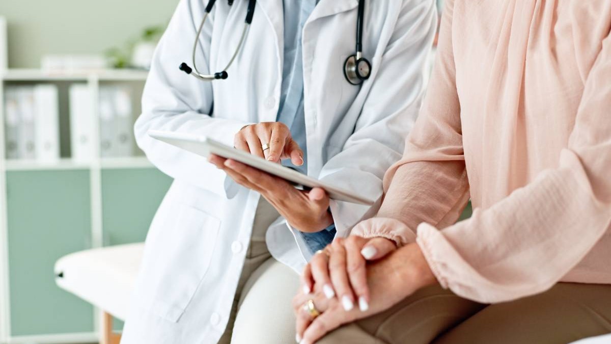 Un medic și o pacientă în timpul consolației, datele sunt digitalizate și pot fi verificate pe o tabletă pe care medicul îi arată ceva femeii.