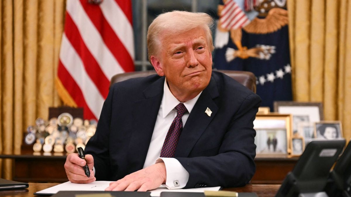 Donald Trump, îmbrăcat în costum, în timp ce stă la Biroul Oval, la Casa Albă, și semnează un document, în ianuarie 2025
