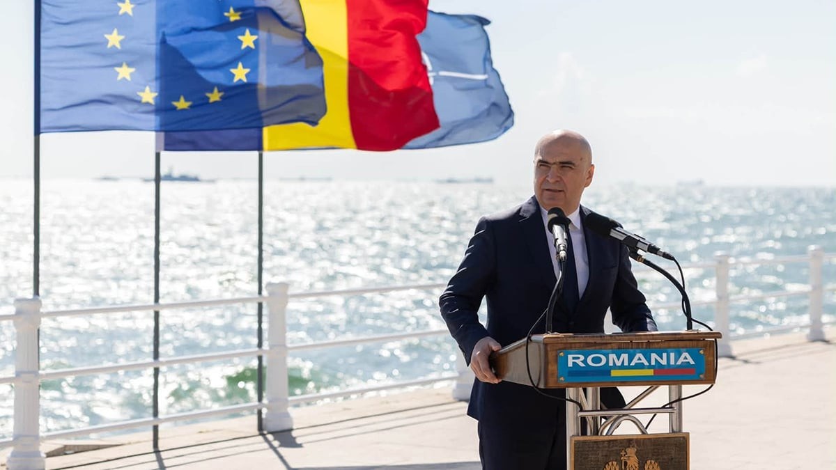 Ilie Bolojan, la Ziua Marinei, pe malul marii avand in spate steagurile UE, Romaniei si NATO