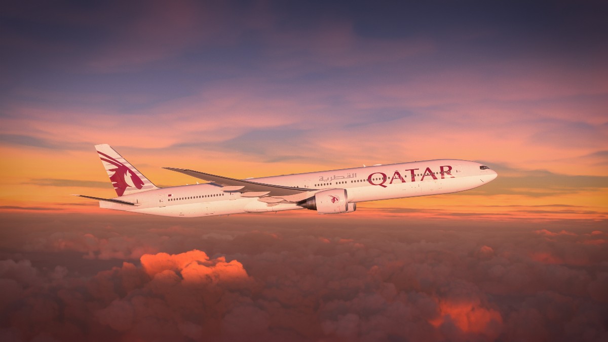 Imaginea aeriană surprinde un avion de pasageri, identificat ca aparținând companiei Qatar Airways după sigla distinctivă, zburând deasupra unui strat gros de nori. Scena este luminată dramatic de culorile unui apus sau răsărit vibrant, care pictează cerul în nuanțe de roșu, portocaliu și violet.