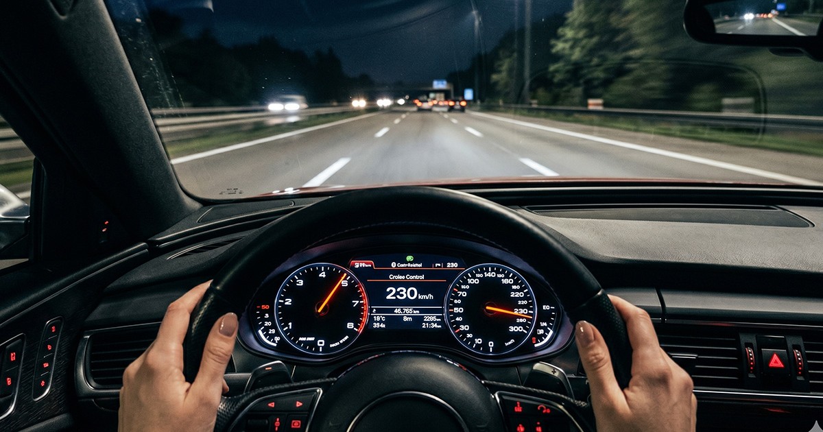 Un volan pe care se află mâinile unei femei iar în fată se află drumul liber iar acul de la vitezometru se află fixat la 230 de km.