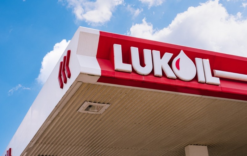 Logo-ul Lukoil cu alb, pe o suprafață roșie. În fundal, cerul este senin.